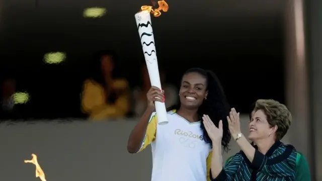 Olympic torch bearer Fabiana Claudino (L), captain of the Brazilian volleyball team, receives the flame from Brazil"s President Dilma Rousseff during the Olympic Flame torch relay at Planalto Palace in Brasilia, Brazil, May 3, 2016