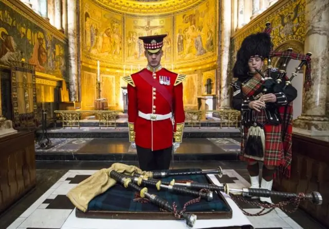 Band Master Will Casson-Smith lays a set of 100-year-old bagpipes as Piper Lance Sergeant John Mitchell (R) plays at The Guards Chapel, Wellington Barracks