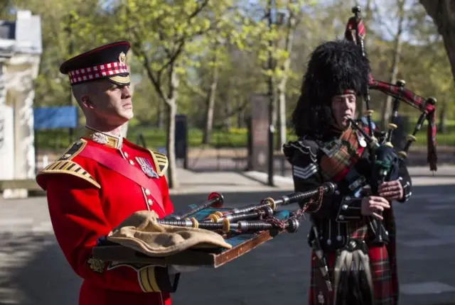 Band Master Will Casson-Smith (L) holds a set of 100-year-old bagpipes as Piper Lance Sergeant John Mitchell (R) plays during a procession at Wellington Barracks