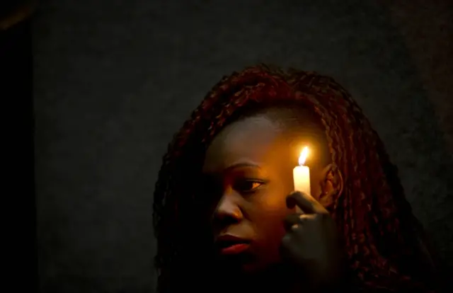 Christine Ochieng holds a candle in memory of those who died in the Garissa University attack, at a memorial service attended by students, relatives and others in Nairobi, Kenya, Saturday, April 2, 2016