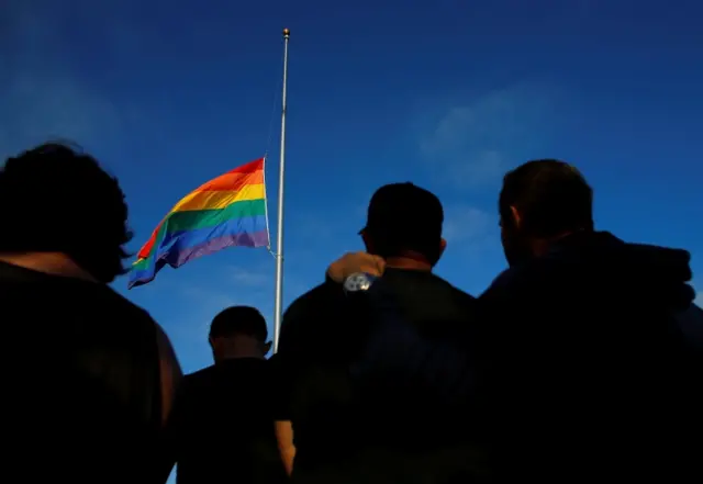 A rainbow flag flies at half mast at a vigil in San Diego, California