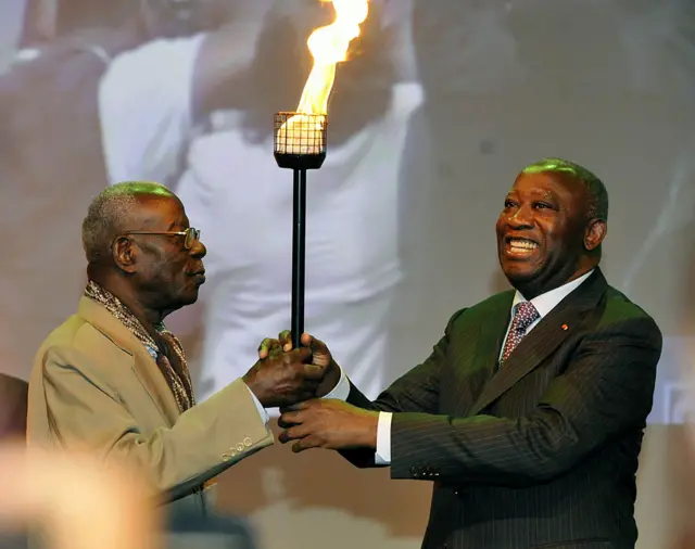 Ivorian writer Bernard Dadie (L) hands over a symbolic torch to Laurent Gbagbo in Abidjan on 9 November 2010