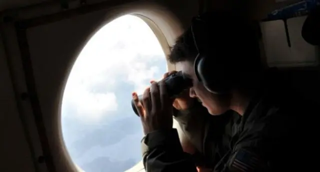 A plane searcher looking out of binoculars from a plane