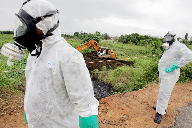 Photo taken on September 19, 2009 of two civil protection workers passing by a bulldozer clearing a site polluted with toxic waste at the Akouedo district in Abidjan.