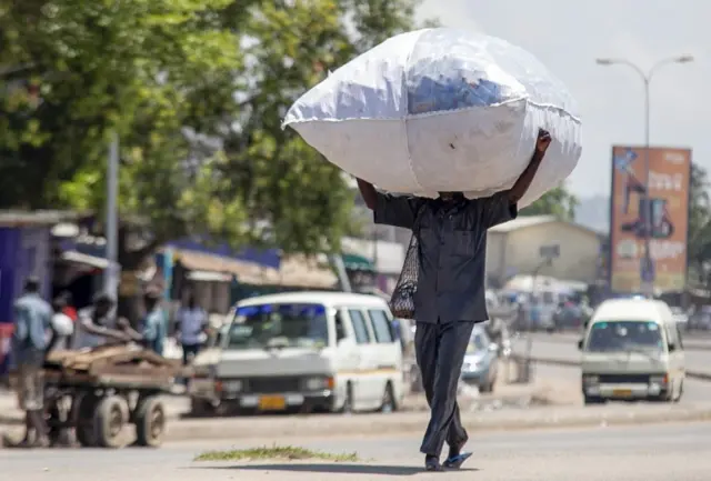 A Ghanaian man walks down a street carrying recyclable plastic bottles in Accra, Ghana