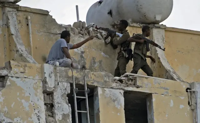 Soldiers with AK47s stand on the damaged exterior of the Ambassador hotel