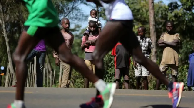 Small group of children watch Kenyan runners go past