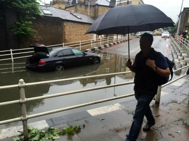 person walking with umbrella and car parked in water