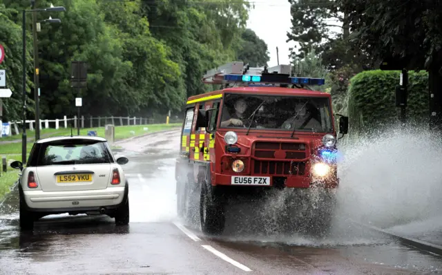 An emergency vehicle going past a car on a flooded road in East Hanningfield, Essex