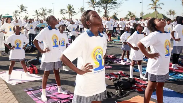 Rows of South African children tilt their heads back as part of an outdoor yoga lesson