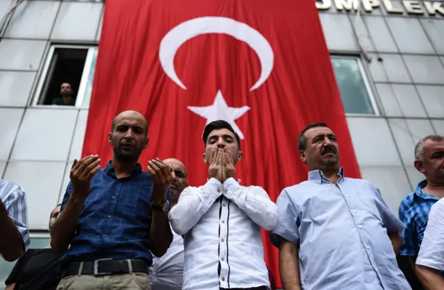 men line up in front of Turkish flag as funeral passes