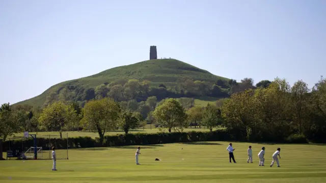 Millfield school children play cricket with Glastonbury Tor in the background