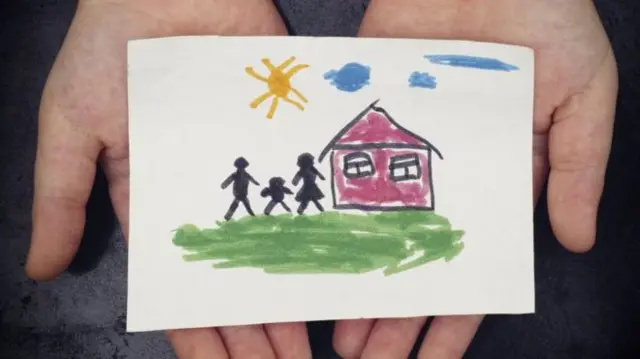 Hands holding a paper with a family drawing