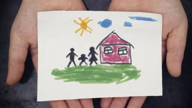 Hands holding drawing of a house and family