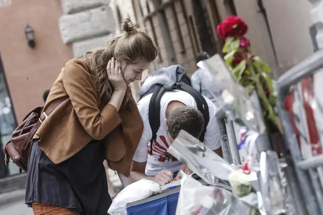 People sign a condolence book at a fence erected outside the French Embassy in Rome, Italy