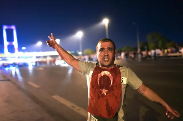 A man covered with blood points at the Bosphorus bridge as Turkish military clashes with people at the entrance to the bridge in Istanbul on July 16, 2016