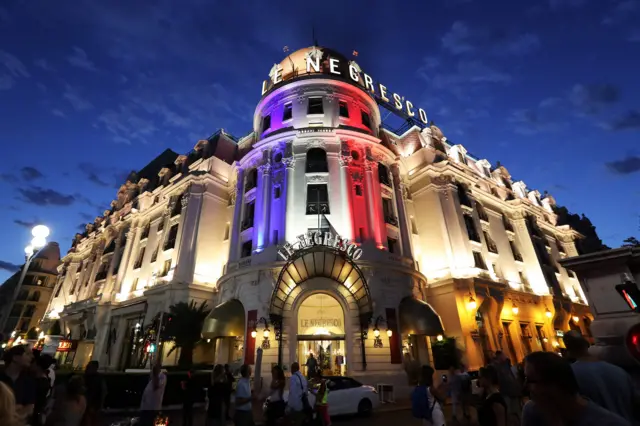 People look at the Negresco Palace in Nice, illuminated with the colours of the French National flag in tribute for the victims of the deadly Bastille Day attack in Nice, on July 15, 2016 in Nice.