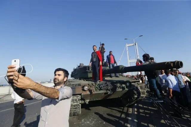 A man takes a selfie in front of a tank