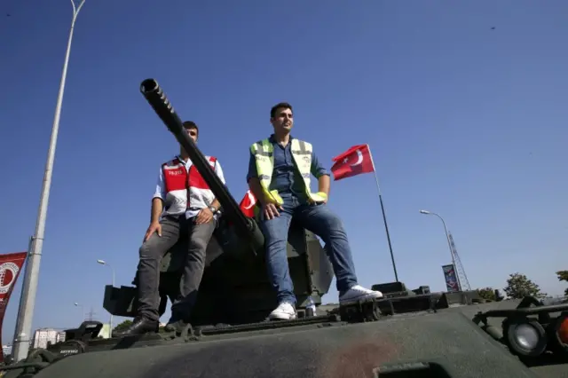 Men sit on top of a military vehicle in front of Sabiha Airport, in Istanbul