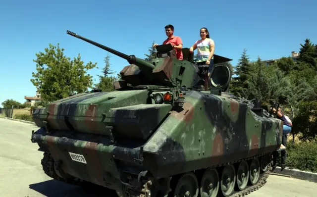 People stand on top of an abandoned armoured vehicle outside the presidential palace in Ankara