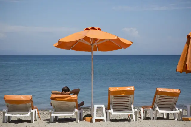 Four sunloungers on a beach, with a parasol