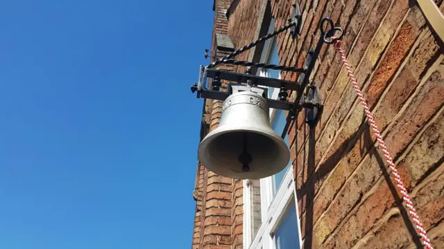 Silver bell mounted hanging from brick wall in sunshine