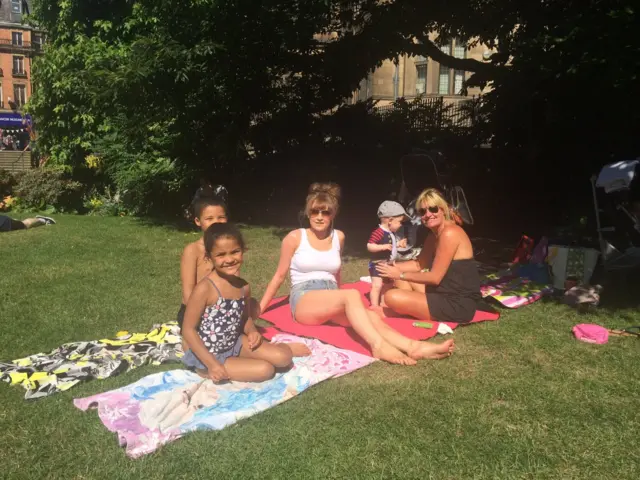 Children sit on grass in Peace Gardens