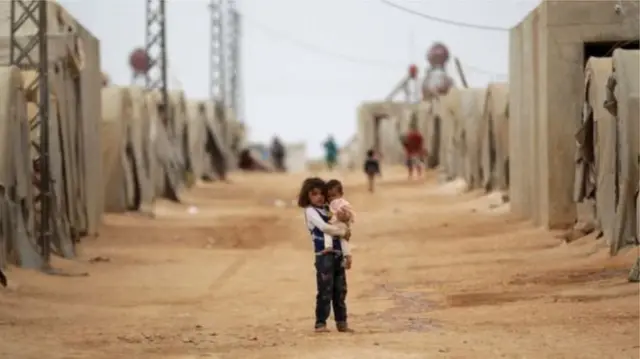 A Syrian child holding another child in a refugee camp