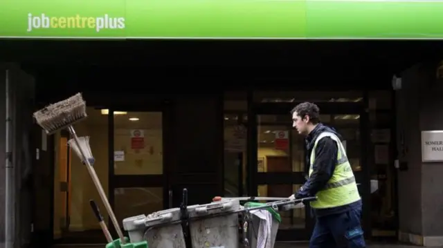 Man wheeling dustcart past job centre