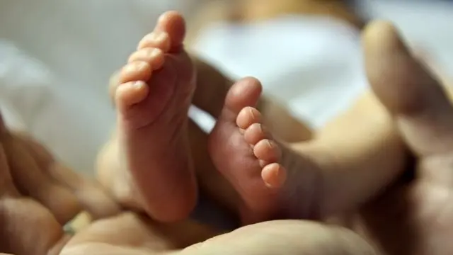 A father cradles the tiny feet of his five-day-old baby girl