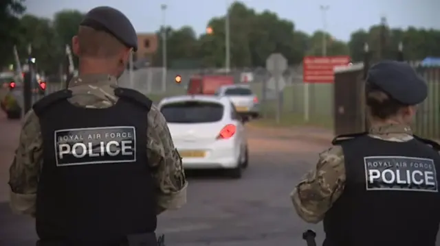 Rear view of two RAF Police officers, man and woman, outside the airbase with vehicles entering