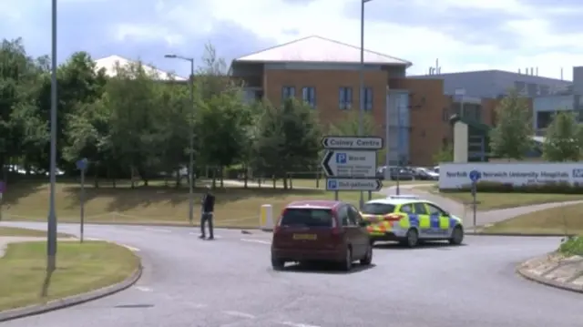 The hospital, as seen from the road, with police car and private vehicle on the road