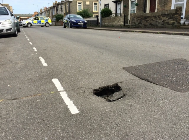 The hole in the road, by the central white lines, with a police car blocking the road