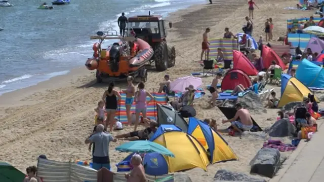 Tractor towing lifeguard dinghy on Sea Palling beach, with beach visitors