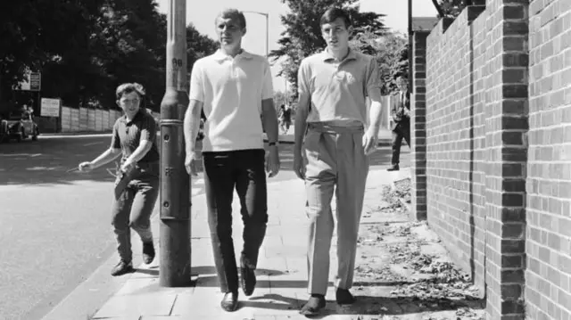 An eager young football fan chases England footballers Bobby Moore and Martin Peters as they stroll near the team's hotel in Hendon, London, on 23 July 1966.