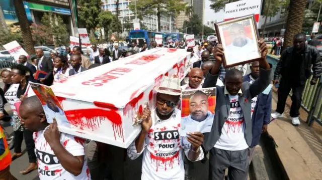 Protesters carry a mock coffin dabbed in red paint