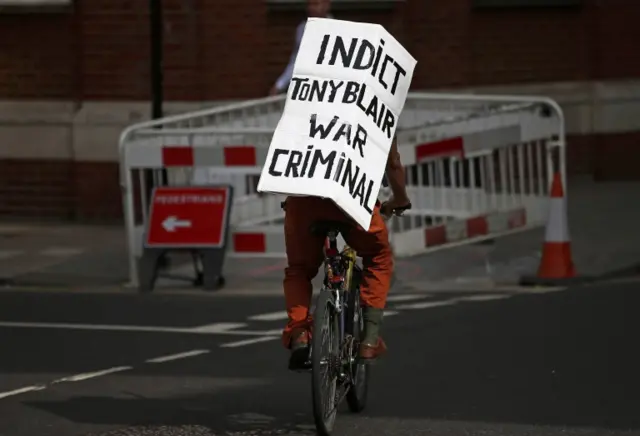 A protester cycles past the Queen Elizabeth II Conference Centre, London, where the publication of the Chilcot inquiry into the Iraq War is taking place