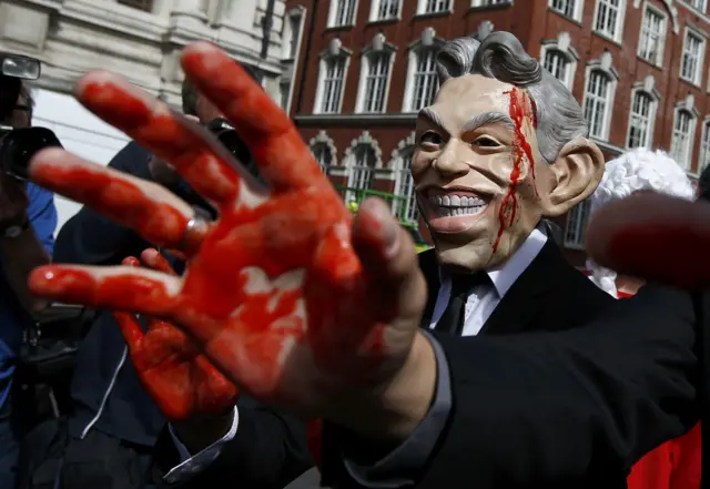 A protester with a Tony Blair mask and red paint