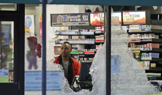 A clerk looks at broken windows shot out at a store