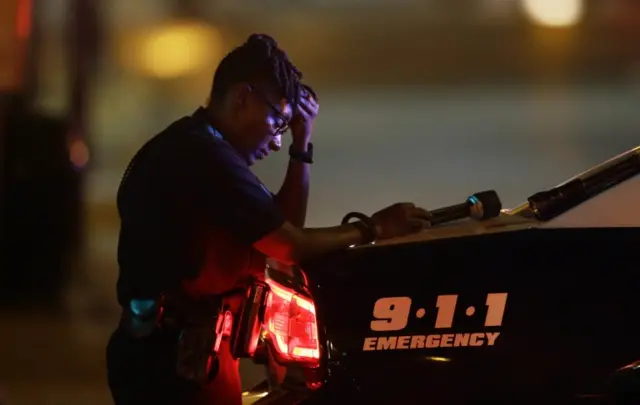 A Dallas police officer, who did not want to be identified, takes a moment as she guards an intersection in the early morning after a shooting