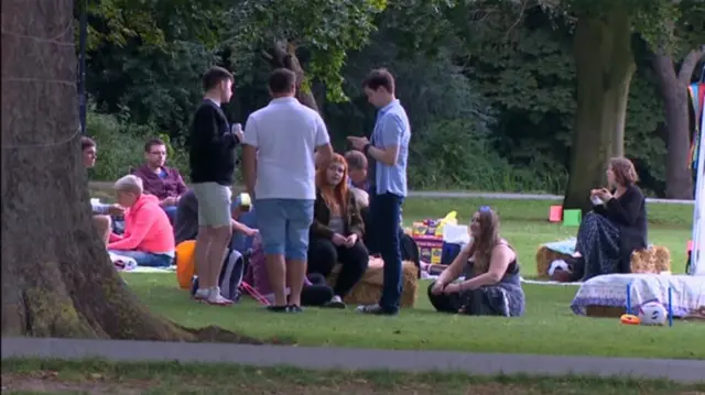 Family and friends sitting, and standing, with picnic hampers, on Jesus Green