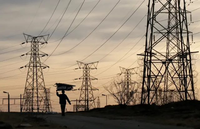 A woman carrying firewood past power lines in South Africa - 2016