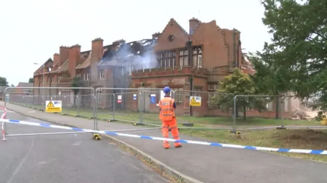 A view of the gutted building, with smoke coming from within, and fencing to barrier it off