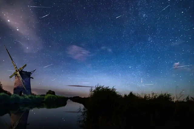 Meteors streaking across the night sky, with a derelict windmill and waterway