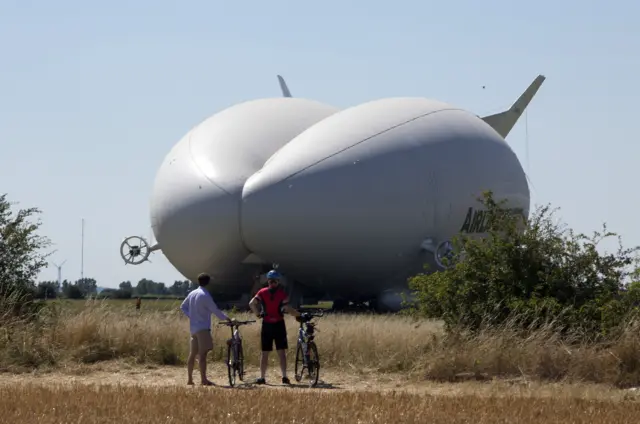 Cyclists look at Airlander in field