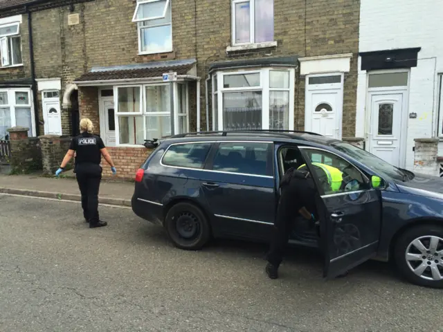 Police search a car outside a house