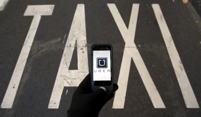 Uber logo on smartphone with Taxi sign painted on road behind