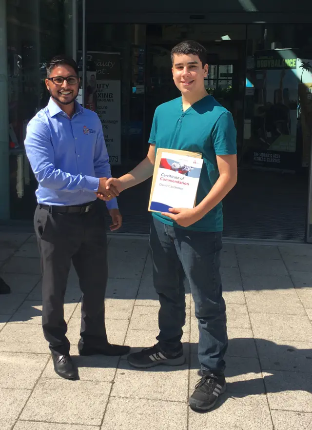 David, in turquoise top and dark jeans, receiving his award from RLSS UK's Aaron Dhanda