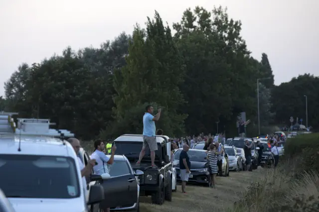 Crowds and cars line the road with spectators taking photographs