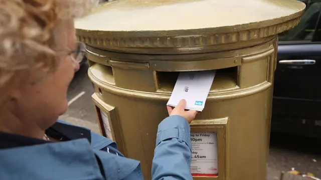 Woman posting into gold postbox